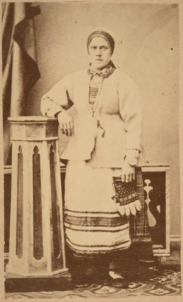 Kansanpukuinen nainen jääskessä. Kädessä koivistolaistyyliset juhlasormikkaat.