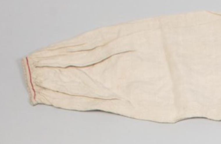 Räisälän paita poimutettu hihansuu ja kapea tikkaus punaisella.