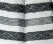 Mustavalkokuva esiliinan nyytingistä, jossa monimutkainen koristekuvio.