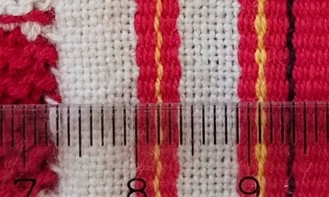 Jääsken kihlakunnan kudonnaisesiliinan ripsiraitoja lähikuvassa, ns. loppuraita esiliinan helmassa.